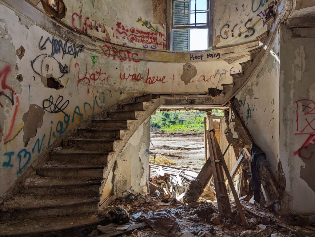 Grand Staircase cluttered with debris from collapsed roof, missing door. 